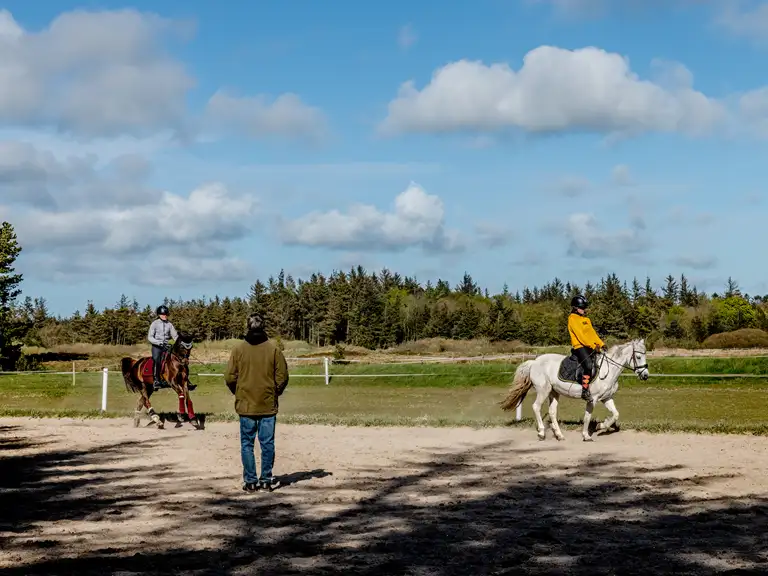 To ryttere, der undervises på udendørs ridebane